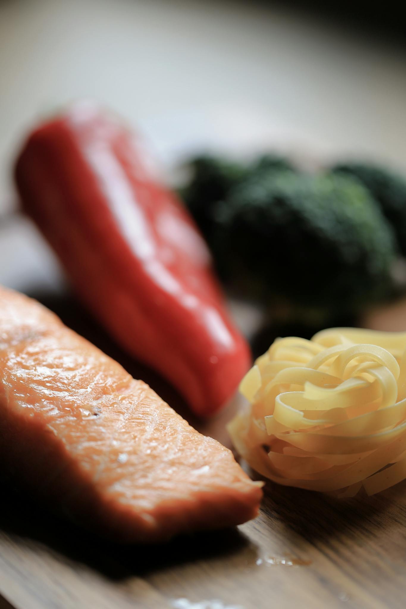 Fresh salmon, bell peppers, and pasta on a wooden surface ready for cooking.